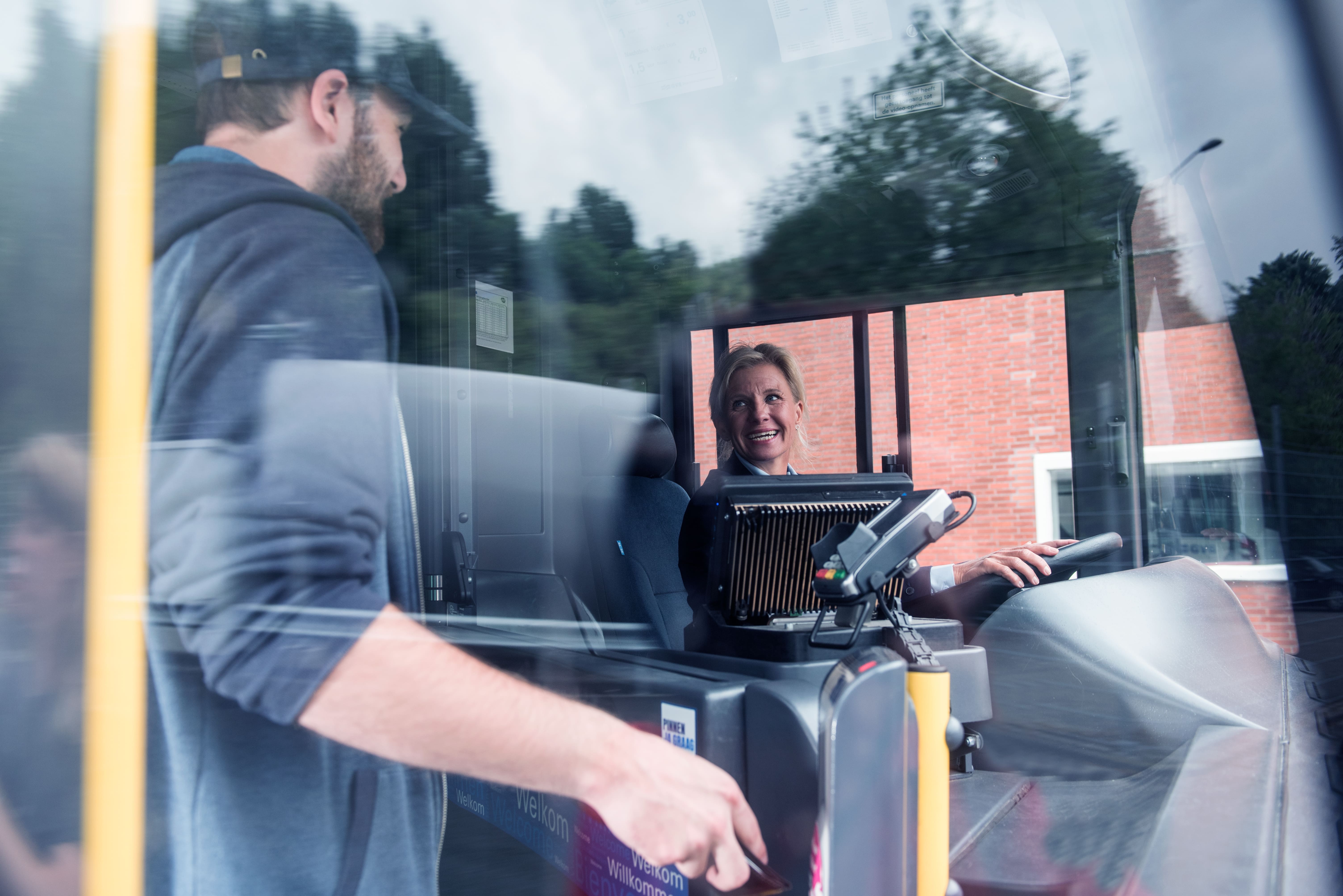 buschauffeur-vrouw-lachend-zittend-in-bus-met-passagier